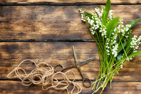 a bouquet of tender lilies of the valley on a wooden scorched background with old scissors and a stick of rope, place for text. Needleworkの写真素材