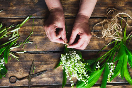 girl knits twine a bouquet of lilies of the valley on a wooden dark background, large stall. Florist makes a delicate bouquet of flowers.の写真素材