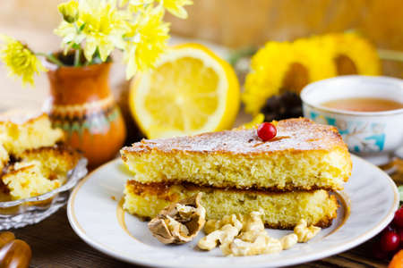 A slice of cake consisting of airy cakes. Homemade cakes with a bright accent on the berry. The composition is complemented by an autumn background consisting of lying sunflowers, a cup of tea, a vase of flowers, lemon.の写真素材