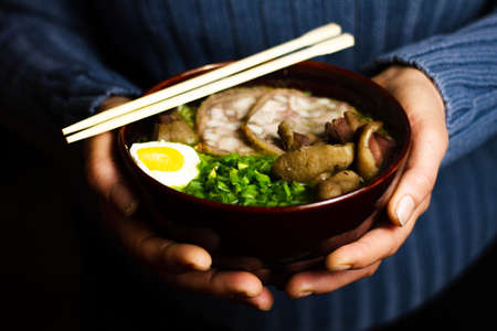 A woman holds a dark bowl with an Asian dish sprinkled with fresh chopped onions. Close-up, vegetarianism concept.の写真素材