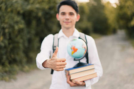 A young European guy in a white dress shirt with a gray backpack on his back holds a stack of...