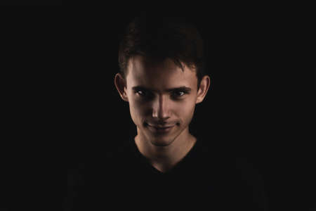 Portrait of a young man wearing a black T-shirt. A man in a black classic sweater on a black background. The dark-haired young man. An enigmatic look.の写真素材