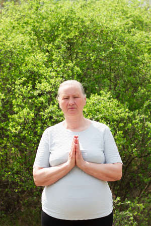 A mature woman, dressed in white clothes, holding hands, resting after yoga alone in the morning. Concentrated on relaxation. Healthy life concept.の写真素材