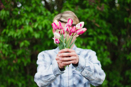 guy in a blue checkered shirt holds a bouquet of pink tulips holding them in front of him, close his face, outdoors.の写真素材