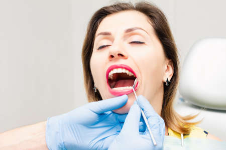 The face of a woman of European appearance with an open mouth at the dentist's office. The doctor works in blue gloves. Close-up.の写真素材
