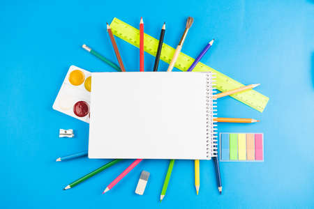 On the colorful school supplies lay a white blank notebook on a blue pastel background. Place for text.の写真素材
