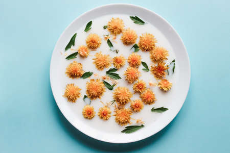 yellow dandelion flowers float in white milk on a flat plate on a pastel blue background, minimalism concept, fashionable layout for trifly flowersの写真素材