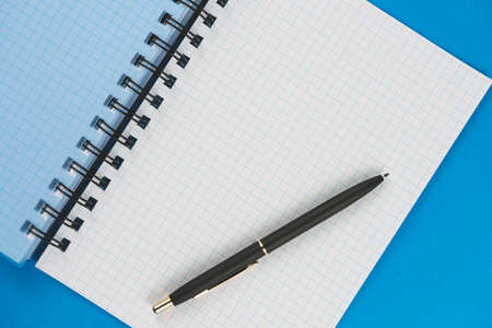 School notebook in a box with a black pen on a blue background. View from above. Place for text.