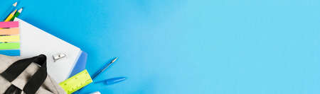 Dropped color school supplies from a gray backpack on a blue background. Photo banner. Place for text.の写真素材