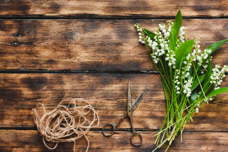 a bouquet of tender lilies of the valley on a wooden scorched background with old scissors and a stick of rope, place for text. Needleworkの写真素材