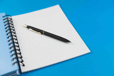 Checkered notebook with a black pen on a blue background. Place for text.の写真素材