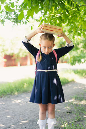 a little girl of European appearance in a dark blue school uniform with pigtails on her head holds with great difficulty a stack of books with a heavy face. Information learning conceptの写真素材