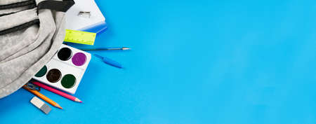 Dropped color school supplies from a gray backpack on a blue background. Photo banner. Place for text.の写真素材