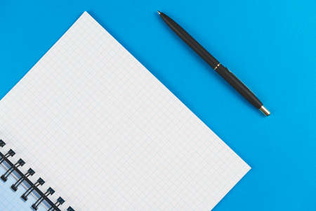 Checkered notebook with a black pen on a blue background. Place for text.の写真素材