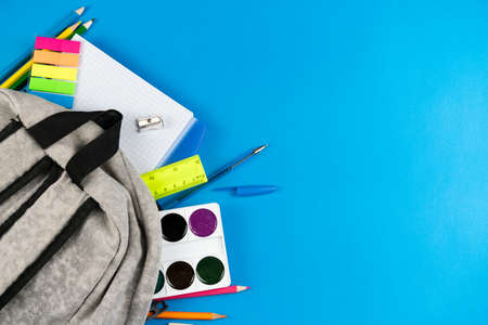 A variety of brightly colored school supplies peep out of a gray schoolbag. View from above. Place for text.の写真素材