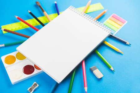 On the colorful school supplies lay a white blank notebook on a blue pastel background. Place for text.の写真素材