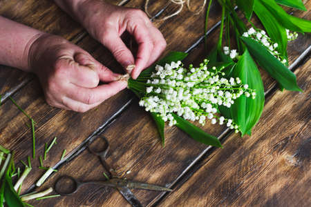 girl knits twine a bouquet of lilies of the valley on a wooden dark background, large stall. Florist makes a delicate bouquet of flowers.の写真素材