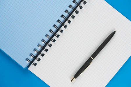 School notebook in a box with a black pen on a blue background. View from above. Place for text.の写真素材