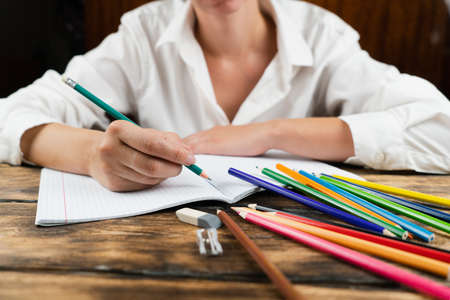 A girl in a white shirt sits at a wooden table with many colorful school supplies. Close-up. School concept.の写真素材