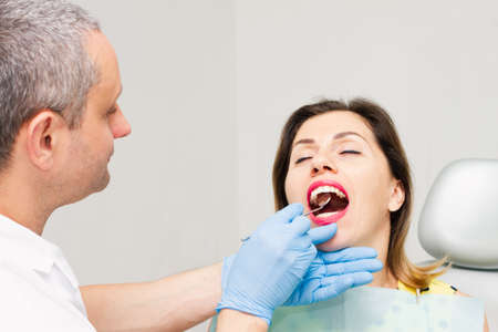 A young woman, wearing a yellow sweater with polka dots, sits at the dentist's office with blue gloves. A healthy smile. Hygiene concept.の写真素材