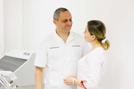 Two professional cheerful doctors, a senior man and a young woman with bright lipstick, dressed in white coats against the background of medical equipment. Health concept.の写真素材
