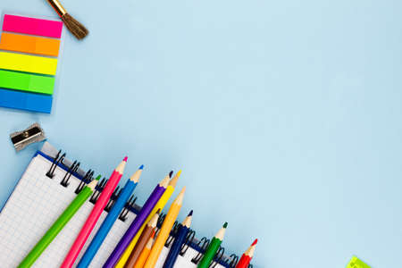 Bright multi-colored pencils lie on a white blank notebook on a blue background. Place for your text. View from above.の写真素材