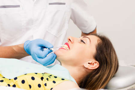 A young, dark-haired woman wearing a yellow polka-dot blouse visits the dentist for the health of her teeth. Close-up. Health concept.の写真素材