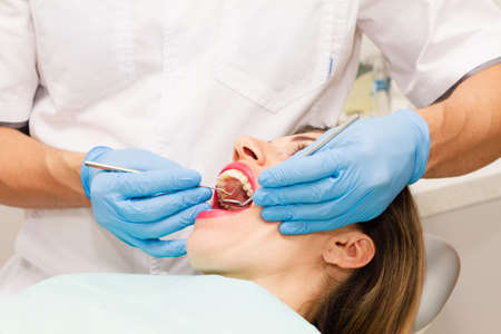 A young, dark-haired woman wearing a yellow polka-dot blouse visits the dentist for the health of her teeth. Close-up. Health concept.の写真素材