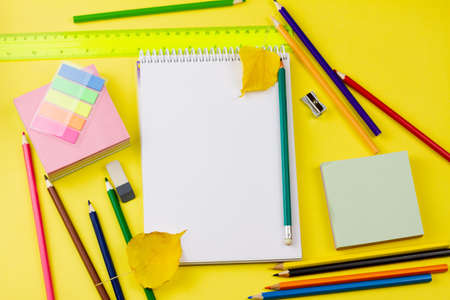 A white blank notebook lies next to many brightly colored school supplies on a yellow background. View from above. Education concept.の写真素材