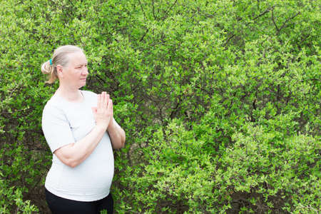 A beautiful adult woman, wearing a white t-shirt, meditates with folded arms. Recreation. Healthy life concept.の写真素材