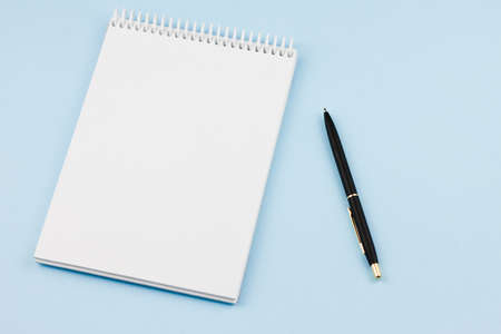 White blank notebook with a black branded pen on a light blue background. View from above. Photo concept.の写真素材