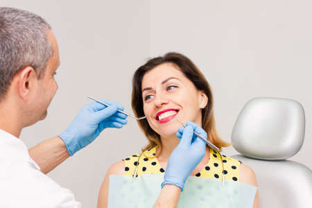 A young woman, wearing a yellow sweater with polka dots, sits at the dentist's office with blue gloves. A healthy smile. Hygiene concept.の写真素材
