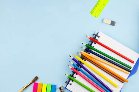 Bright multi-colored pencils lie on a white blank notebook on a blue background. Place for your text. View from above.の写真素材