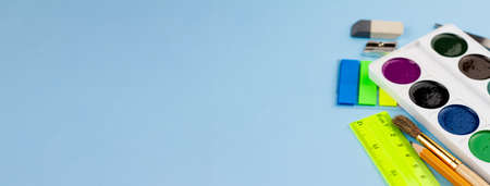 Watercolor paints lie on the stationery on a blue background. Photo banner. Place for your text. View from above.の写真素材