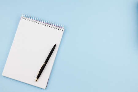 White blank notebook with a black branded pen on a light blue background. View from above. Photo concept.の写真素材