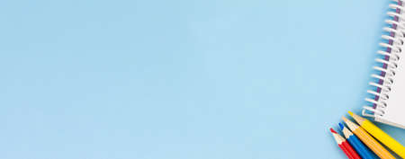 White blank notebook with colored pencils on a blue background. Banner photo. Place for your text. View from above. Education concept.の写真素材