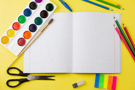A blank checkered notebook lies with school supplies on a yellow background. View from above. Education concept.の写真素材
