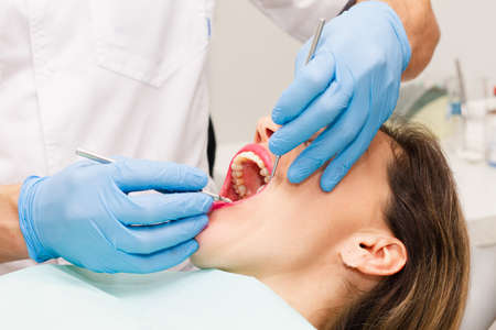 The face of a beautiful dark-haired woman with red lipstick and an open mouth. Doctor's appointment with blue gloves. Health concept.の写真素材