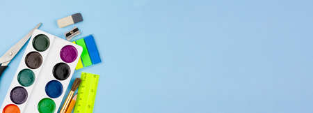Watercolor paints lie on the stationery on a blue background. Photo banner. Place for your text....