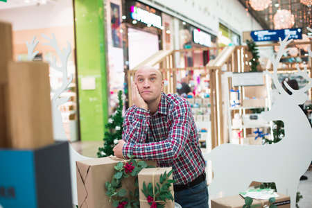 Cheerful handsome adult man, dressed in a plaid shirt and jeans, holds gift boxes and looks at the camera.の写真素材