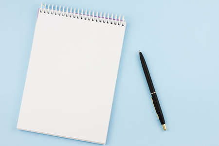White blank notebook with a black branded pen on a light blue background. View from above. Photo concept.の写真素材