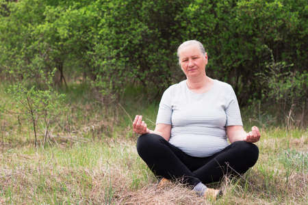 Portrait of a senior woman, wearing a white T-shirt and black pants, meditates in nature. Meditation, yoga and relaxation concept.の写真素材