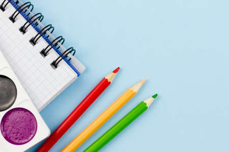 Notebook with colored pencils and paint on a blue background. Place for your text. View from above....