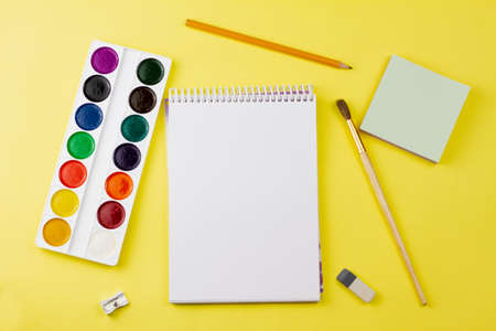 Blank notebook with colored paint and other supplies on a yellow background. View from above. Place for your text.の写真素材