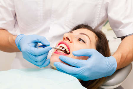 The face of a beautiful dark-haired woman with red lipstick and an open mouth. Doctor's appointment with blue gloves. Health concept.の写真素材