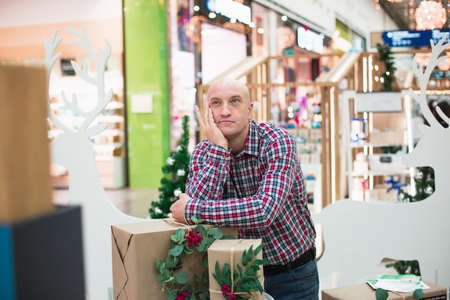 Cheerful handsome adult man, dressed in a plaid shirt and jeans, holds gift boxes and looks at the camera.の写真素材