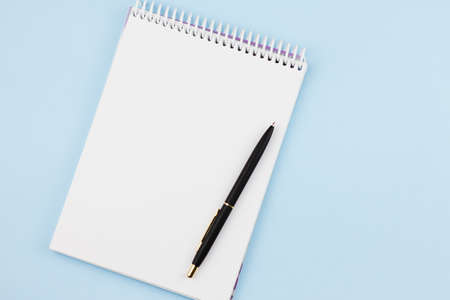 White blank notebook with a black branded pen on a light blue background. View from above. Photo concept.の写真素材