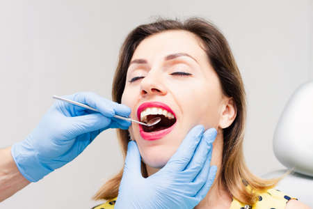 The face of a beautiful dark-haired woman with red lipstick and an open mouth. Doctor's appointment with blue gloves. Health concept.の写真素材