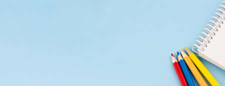 White blank notebook with colored pencils on a blue background. Banner photo. Place for your text. View from above. Education concept.の写真素材