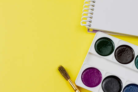 Blank notebook with colored paint and other supplies on a yellow background. View from above. Place for your text.の写真素材